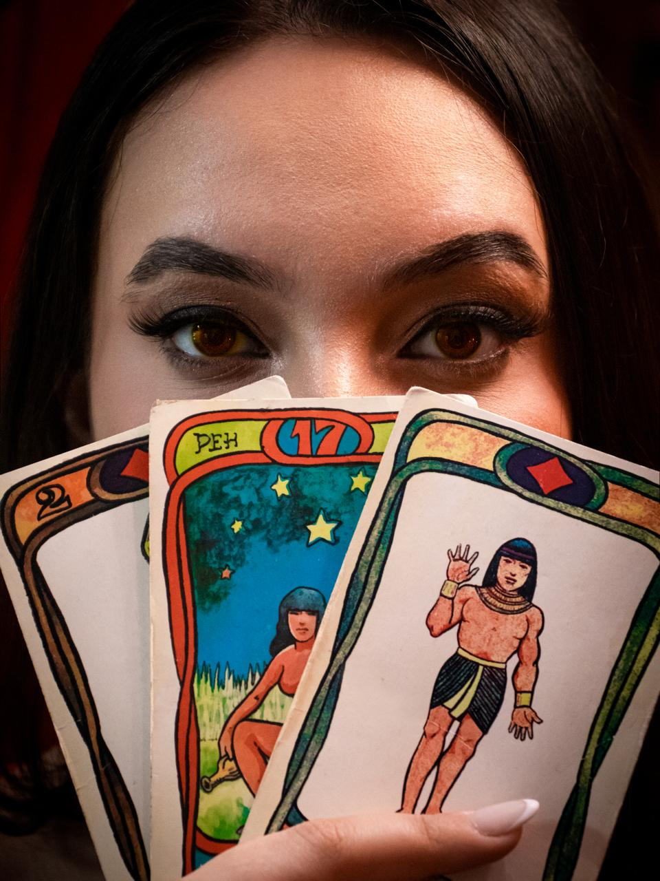 Vidente Samanta olhando por trás de cartas de tarot abertas em leque